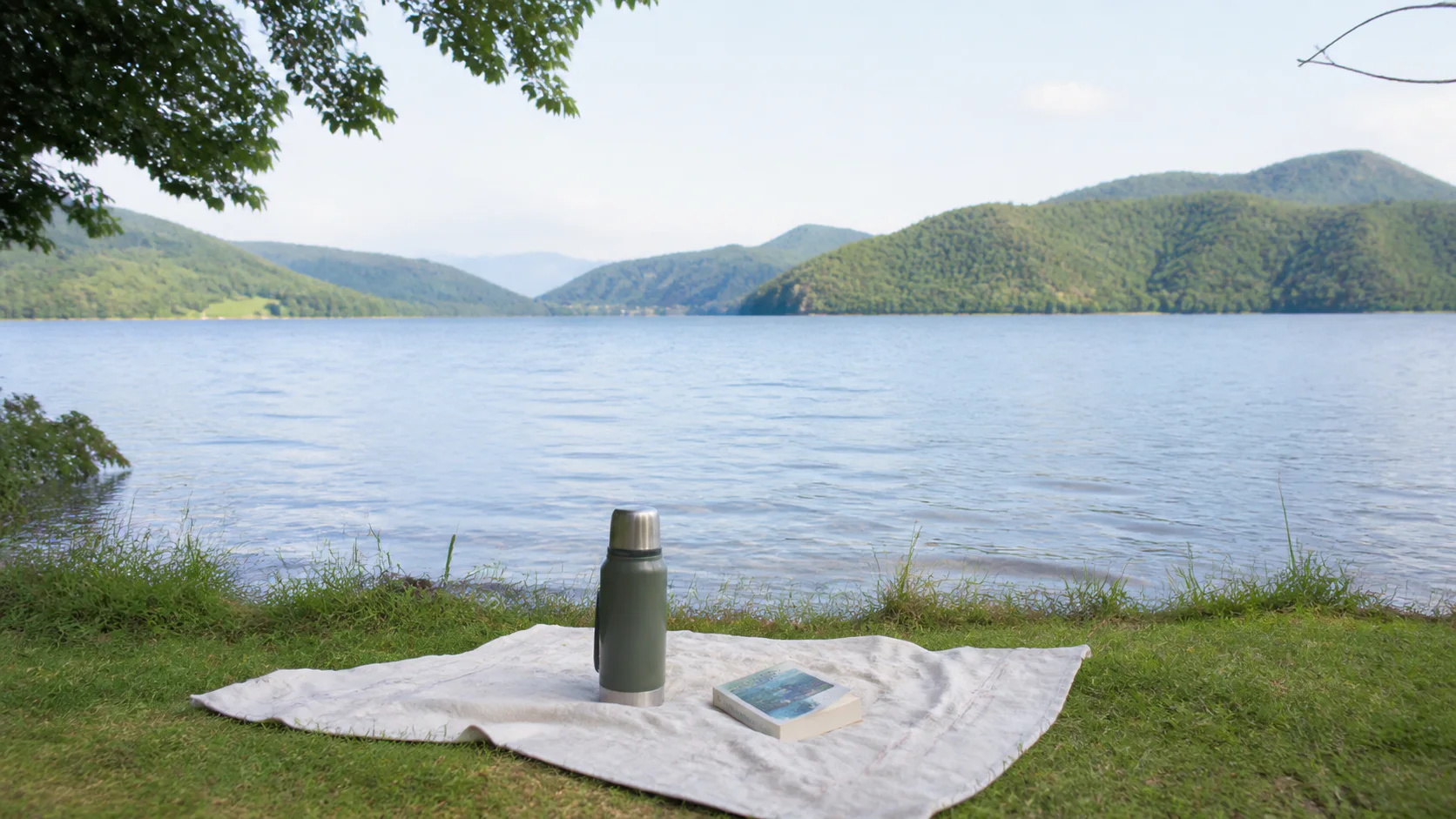 湖畔で本と温かい飲み物を楽しむひとり旅の風景